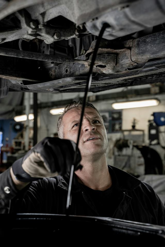 Een mechanieker kijkt onder een wagen op de brug
